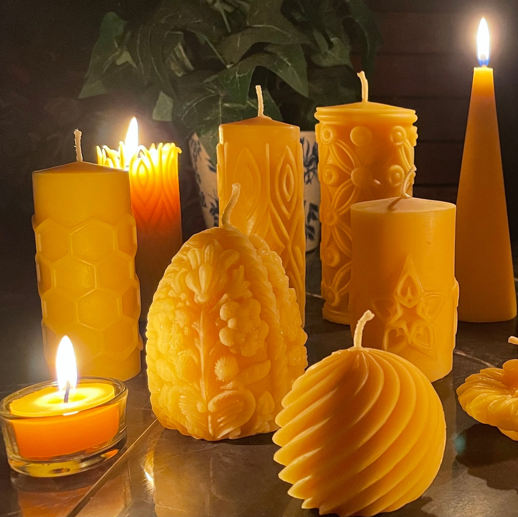 Collection of various yellow candles with intricate designs on a reflective surface.