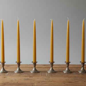 Six yellow beeswax candles in silver candle holders on a wooden table.