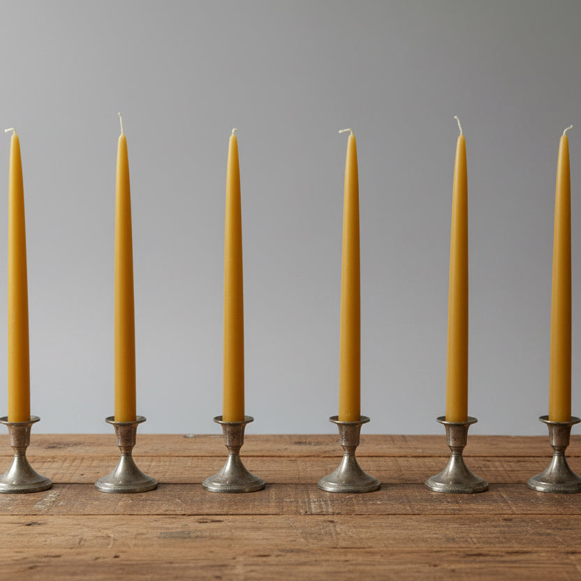 Six yellow beeswax candles in silver candle holders on a wooden table.