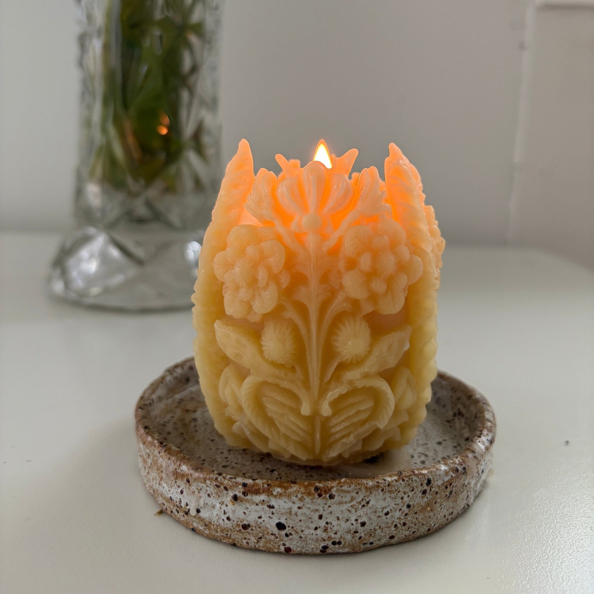 Decorative candle with floral design in a holder on a white surface