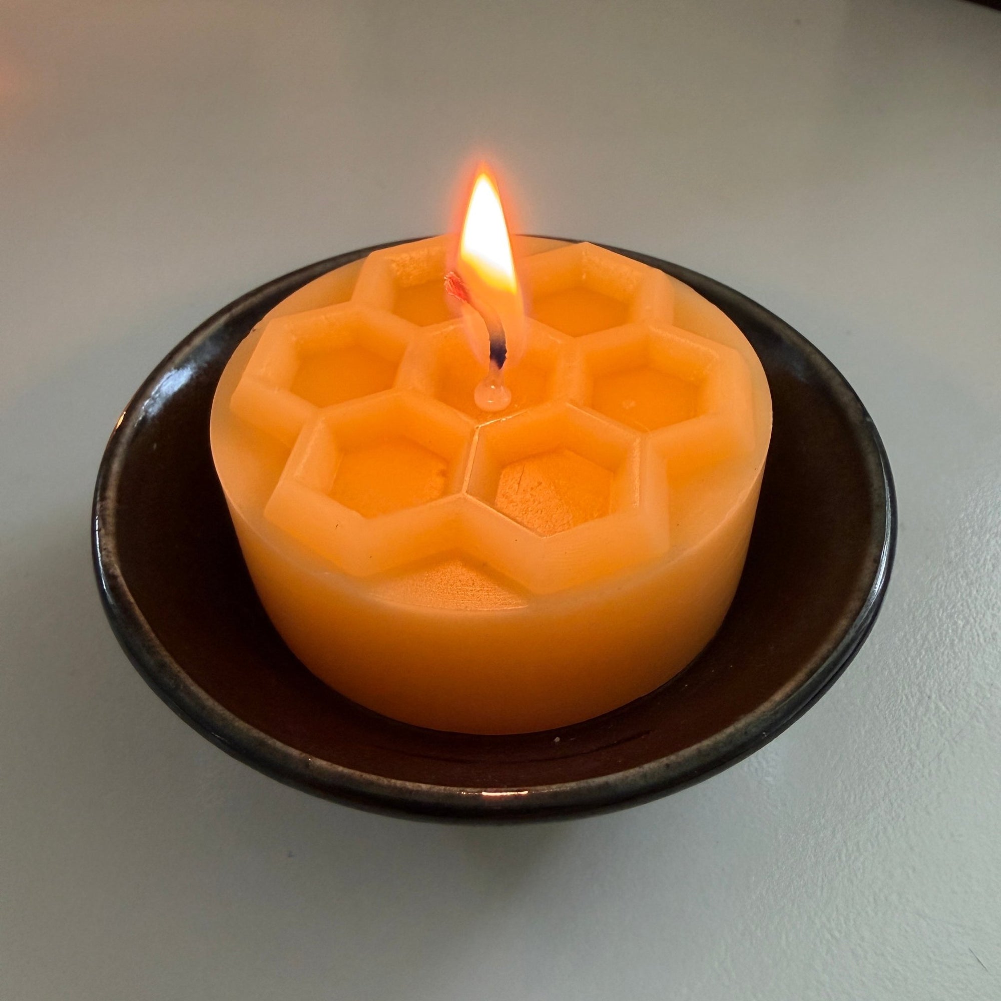 Hexagonal honeycomb-patterned beeswax candle burning on a ceramic plate