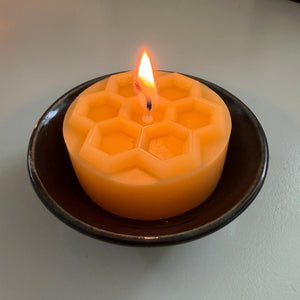 Hexagonal honeycomb-patterned beeswax candle burning on a ceramic plate