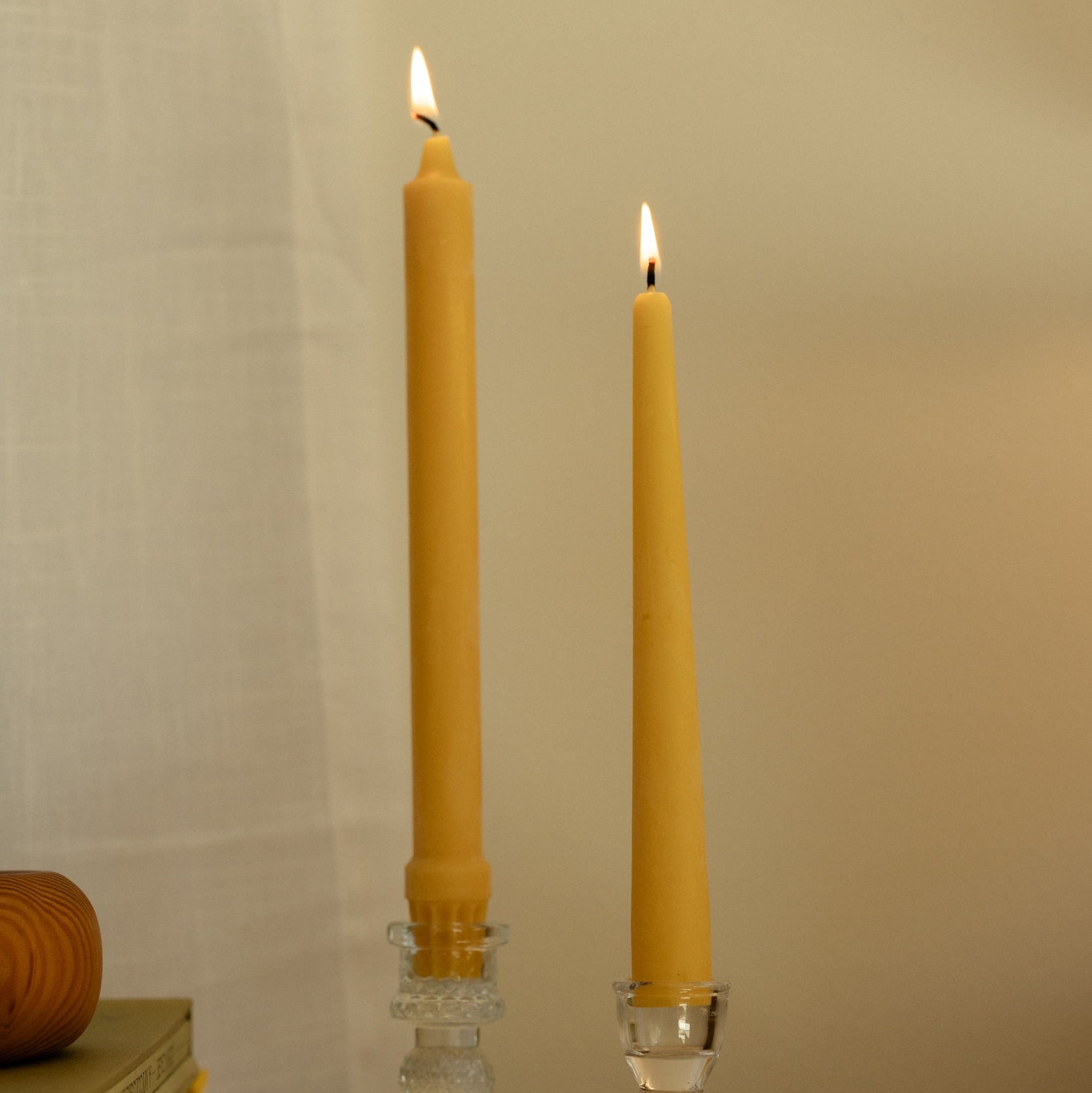 Two lit candles in glass holders on a wooden surface with a neutral background