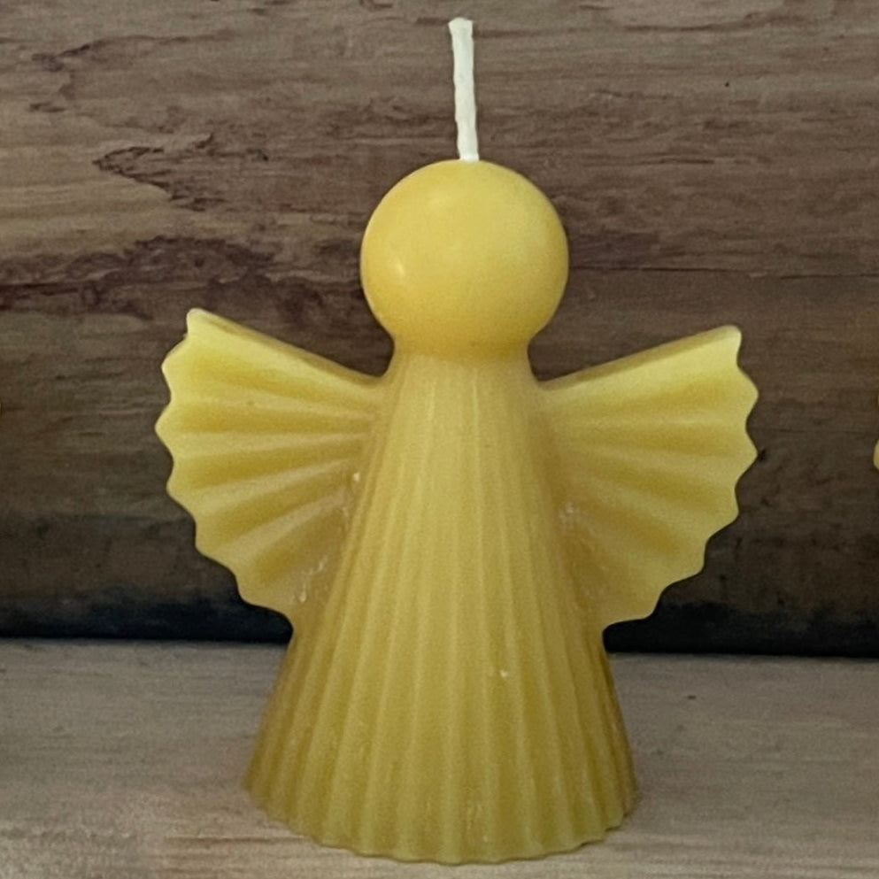 angel-shaped beeswax candle on a wooden surface 