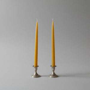 Two yellow candles in silver candle holders on a white background