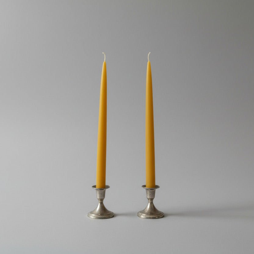 Two yellow candles in silver candle holders on a white background